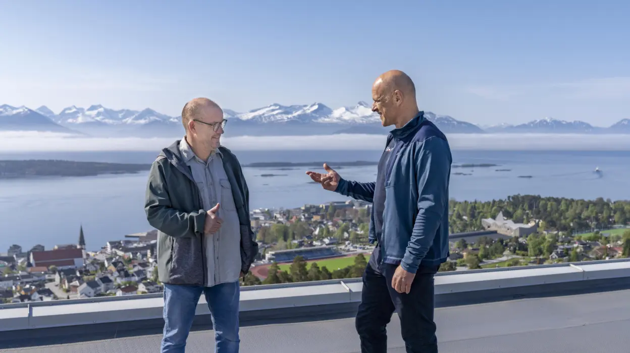 To menn på toppen av høy bygning. Fjord og fjell i bakgrunnen.