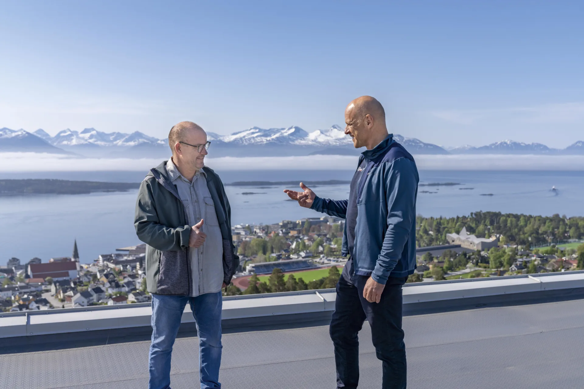 To menn på toppen av høy bygning. Fjord og fjell i bakgrunnen.