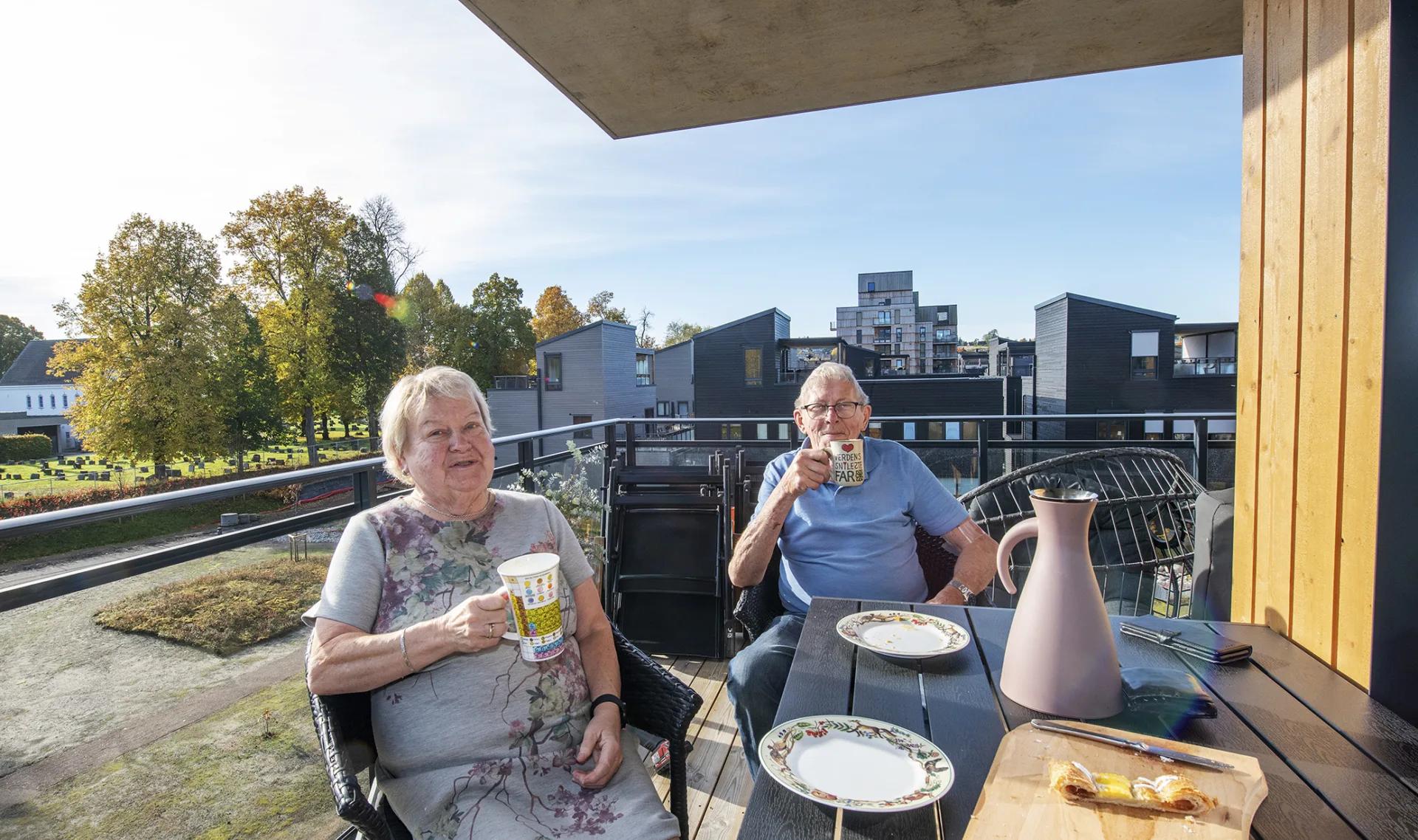 Eldre mann og kvinne drikker kaffe i sola på altanen