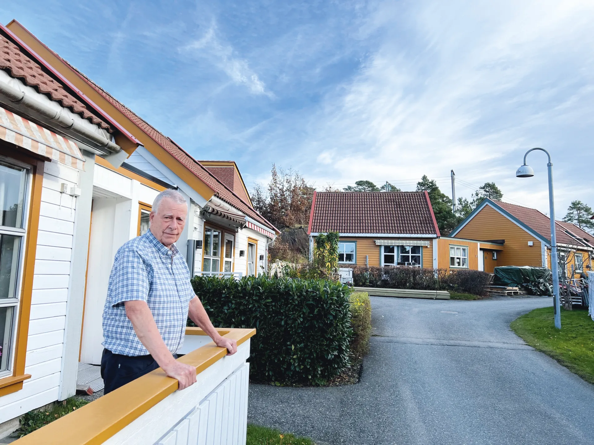 Eldre man står utenfor sim bolig og ser fornøyd in i kamera