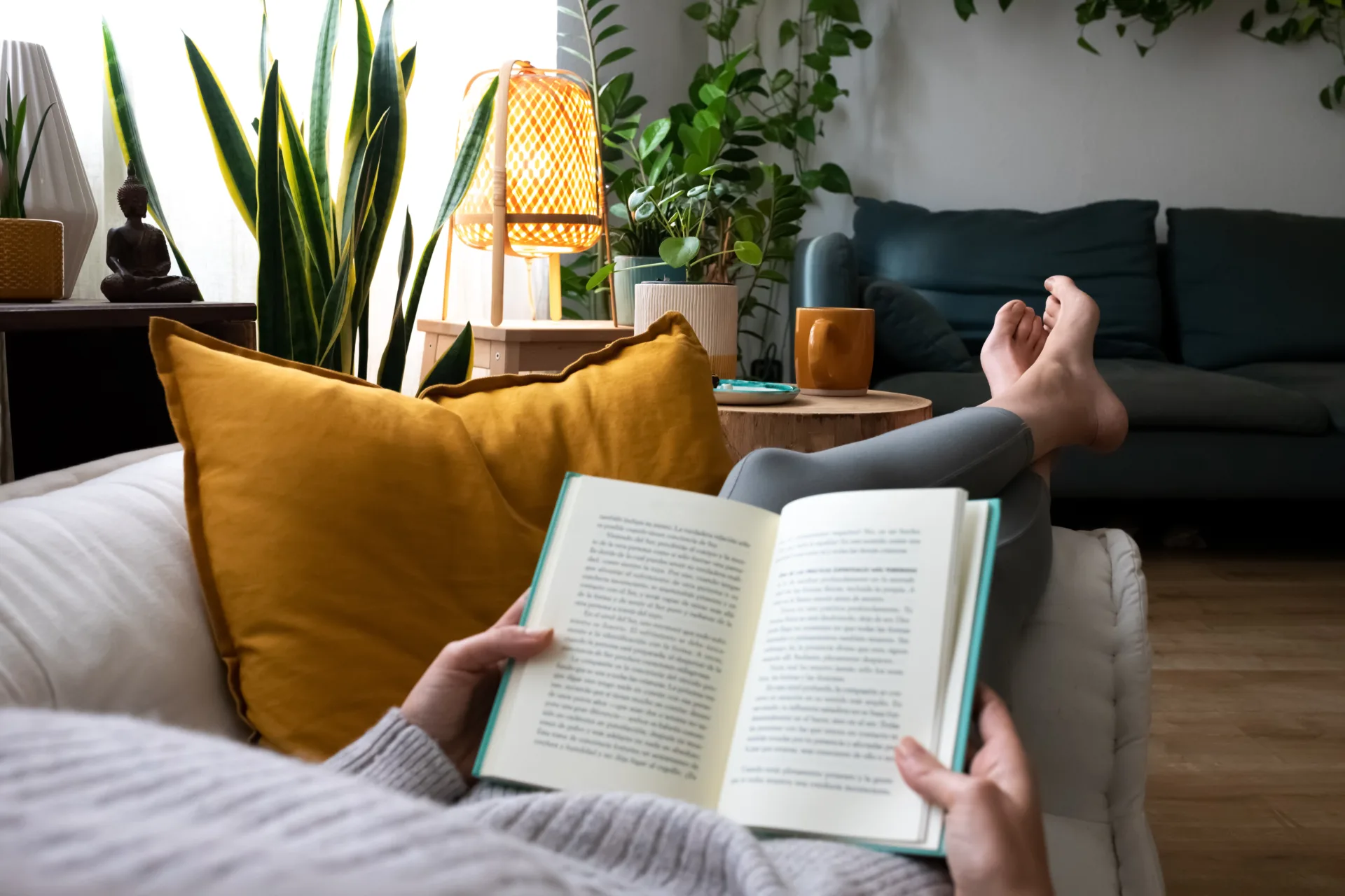 En voksen kvinne ligger på en sofa og leser en bok.